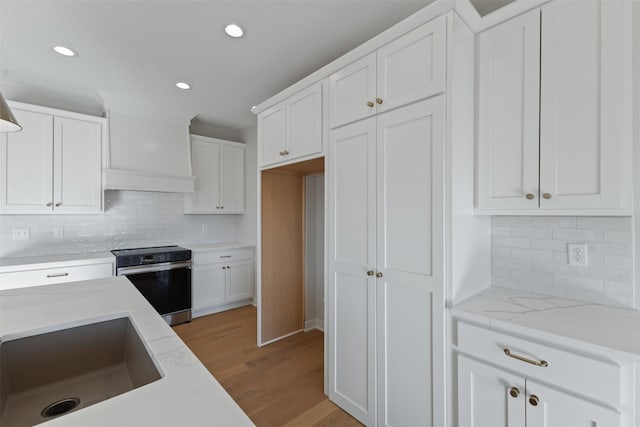 kitchen featuring premium range hood, white cabinetry, backsplash, and stainless steel electric range oven