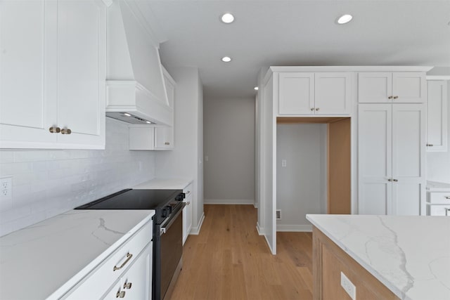 kitchen featuring stainless steel range with electric cooktop, custom exhaust hood, white cabinetry, and light stone counters