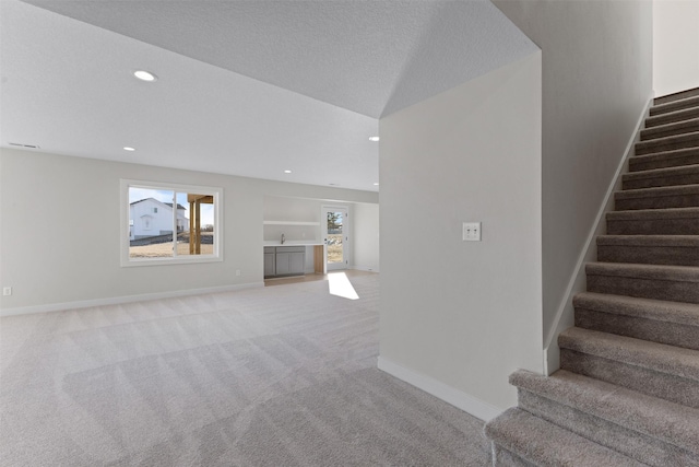 unfurnished living room featuring sink, a textured ceiling, and light carpet