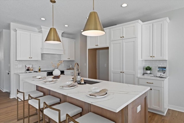 kitchen featuring white cabinetry, sink, decorative light fixtures, and a kitchen island with sink