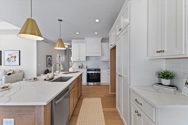 kitchen featuring a center island with sink, appliances with stainless steel finishes, pendant lighting, light stone countertops, and white cabinets