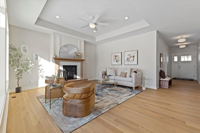 living room featuring light hardwood / wood-style floors, a raised ceiling, and ceiling fan