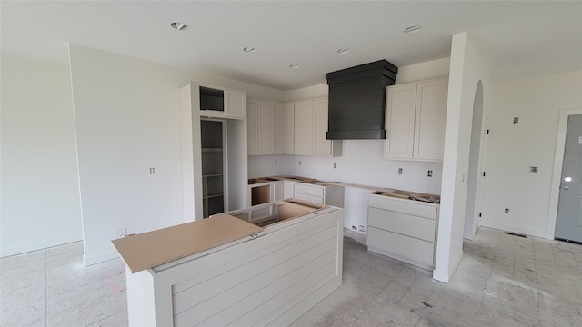 kitchen featuring a center island, wall chimney range hood, and white cabinets