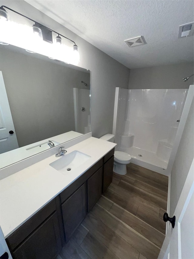 bathroom featuring hardwood / wood-style floors, vanity, toilet, a textured ceiling, and walk in shower