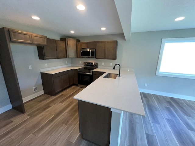 kitchen with sink, dark wood-type flooring, kitchen peninsula, dark brown cabinets, and appliances with stainless steel finishes