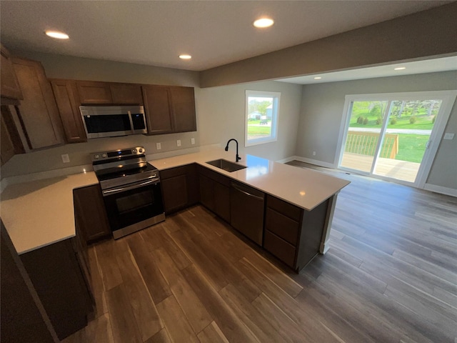 kitchen with kitchen peninsula, dark hardwood / wood-style flooring, stainless steel appliances, and sink