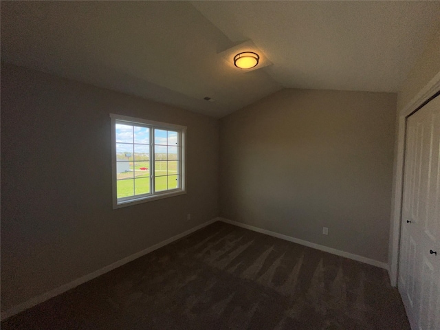 unfurnished bedroom with dark carpet, lofted ceiling, and a closet