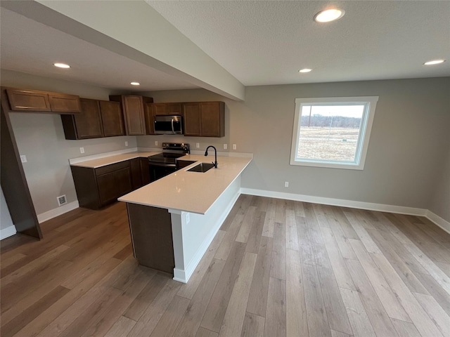 kitchen with a peninsula, a sink, electric stove, light countertops, and stainless steel microwave