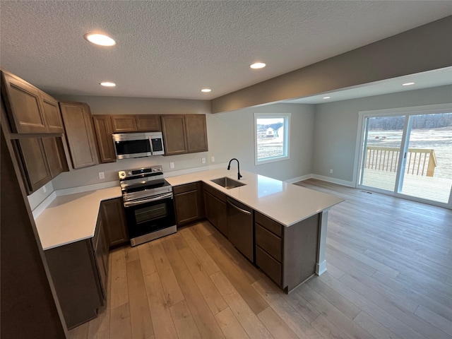 kitchen featuring light wood-style flooring, appliances with stainless steel finishes, a peninsula, light countertops, and a sink