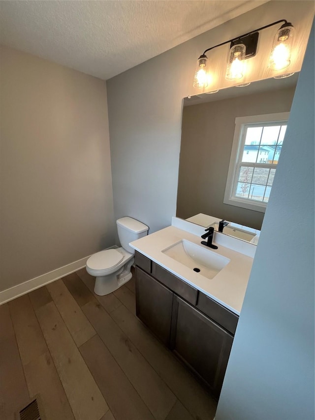 half bath with a textured ceiling, toilet, wood finished floors, vanity, and baseboards