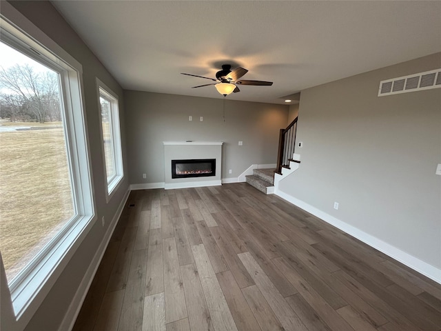 unfurnished living room featuring visible vents, stairway, a glass covered fireplace, wood finished floors, and baseboards