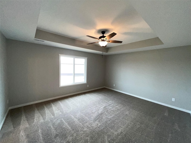 spare room featuring dark carpet, baseboards, a raised ceiling, and a ceiling fan