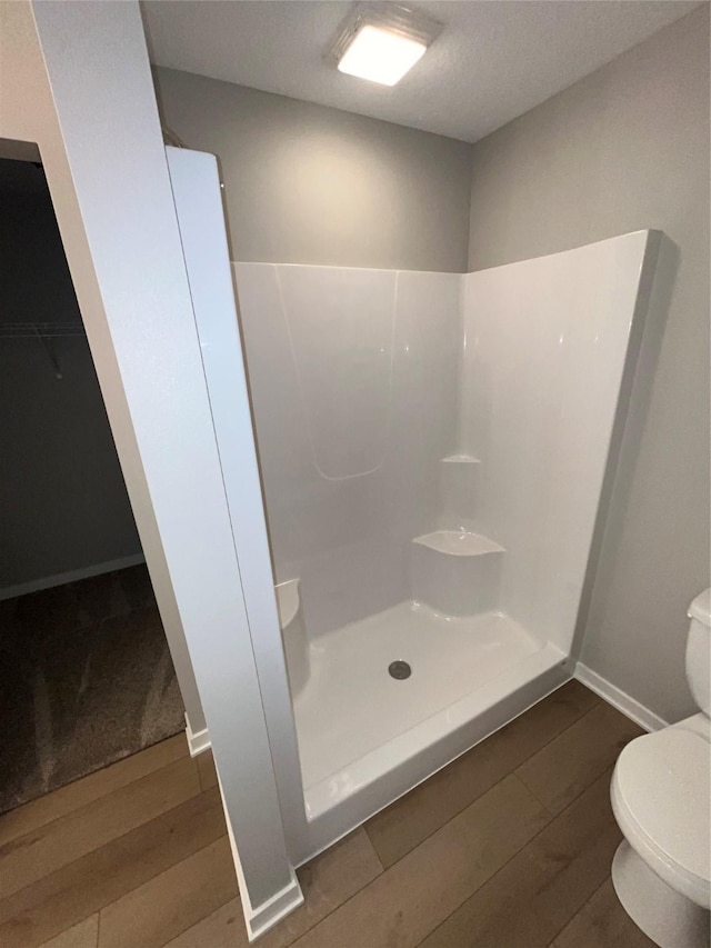 bathroom featuring a stall shower, baseboards, toilet, and wood finished floors