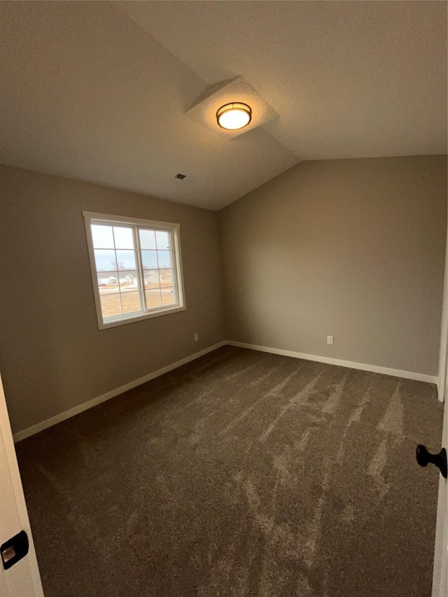 spare room with vaulted ceiling, dark carpet, and baseboards