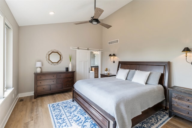 bedroom with high vaulted ceiling, ceiling fan, a barn door, and light hardwood / wood-style floors