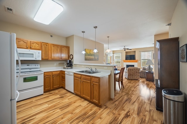 kitchen featuring light wood-style floors, open floor plan, a sink, white appliances, and a peninsula