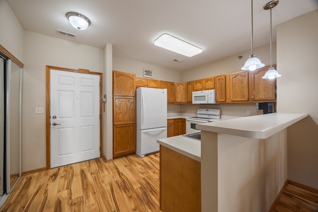 kitchen with a peninsula, white appliances, light wood-style floors, hanging light fixtures, and light countertops