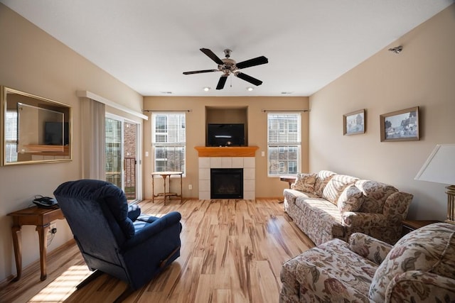 living room featuring plenty of natural light, light wood-style flooring, a ceiling fan, and a tile fireplace