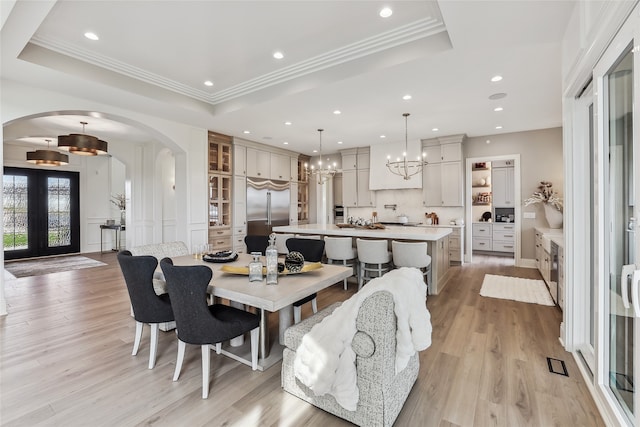 dining room featuring french doors, a raised ceiling, a chandelier, light wood-type flooring, and ornamental molding