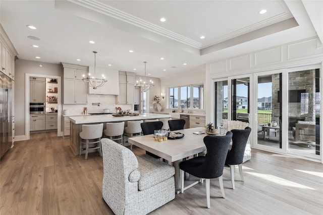 dining room with light wood-type flooring, ornamental molding, a tray ceiling, sink, and an inviting chandelier