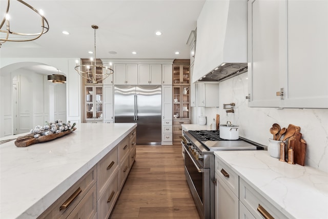 kitchen featuring white cabinets, premium appliances, premium range hood, and hanging light fixtures