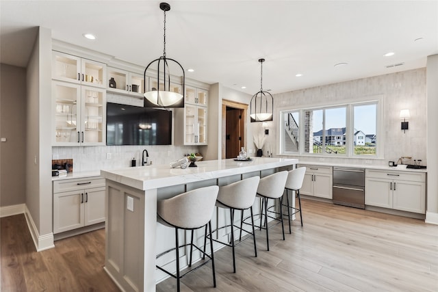 kitchen featuring backsplash, white cabinets, hanging light fixtures, light hardwood / wood-style flooring, and a kitchen bar