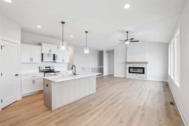 kitchen with ceiling fan, sink, stainless steel appliances, an island with sink, and white cabinets