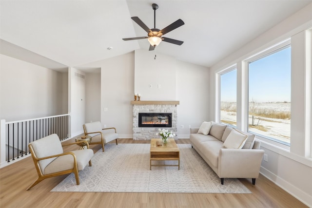 living area with light wood-type flooring, baseboards, a stone fireplace, and lofted ceiling