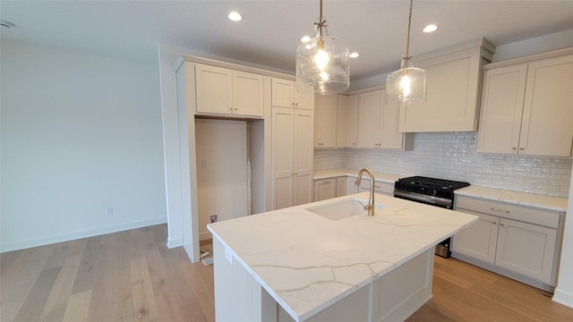 kitchen with stainless steel gas range, a center island with sink, light stone counters, and sink