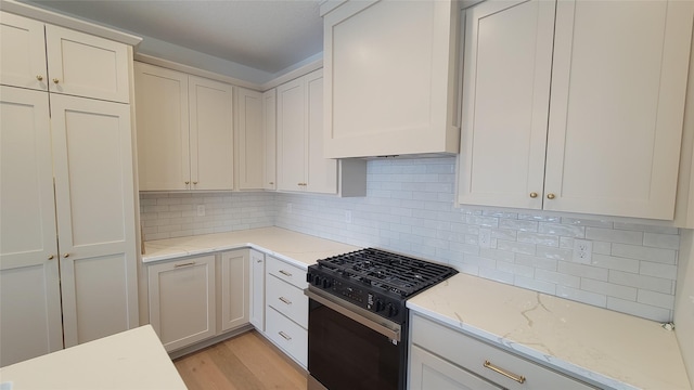 kitchen with light stone countertops, white cabinetry, tasteful backsplash, light hardwood / wood-style flooring, and black gas stove