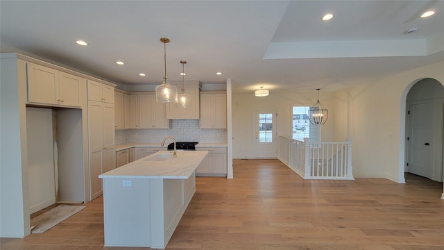 kitchen with decorative backsplash, a kitchen island with sink, sink, light hardwood / wood-style floors, and hanging light fixtures