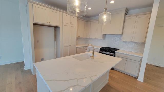 kitchen with a center island with sink, sink, hanging light fixtures, light stone countertops, and stainless steel range with gas stovetop