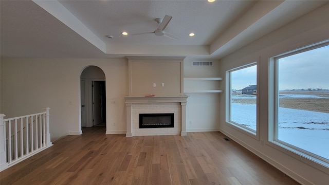 unfurnished living room with a raised ceiling, a water view, ceiling fan, a fireplace, and light hardwood / wood-style floors