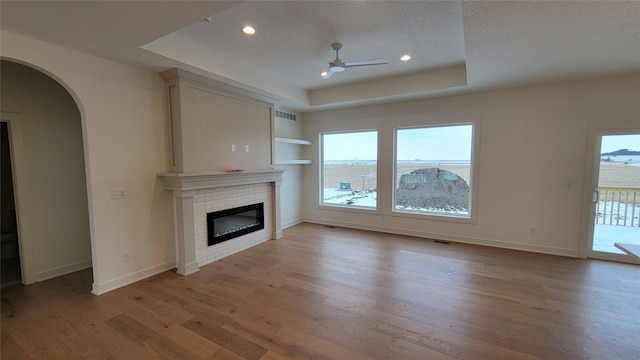 unfurnished living room featuring a tray ceiling, built in shelves, a fireplace, and a textured ceiling