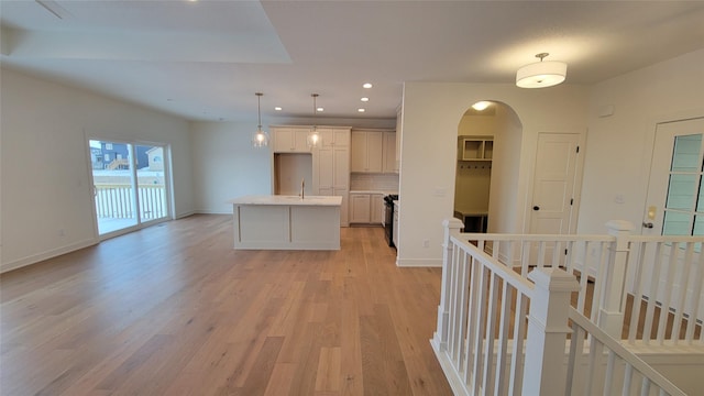 kitchen featuring pendant lighting, a center island with sink, sink, decorative backsplash, and light hardwood / wood-style floors