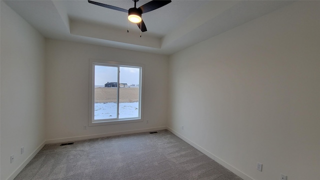 spare room featuring a tray ceiling, ceiling fan, and light colored carpet