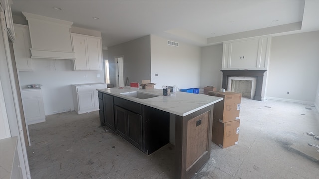 kitchen featuring light stone countertops, a center island with sink, white cabinetry, and sink