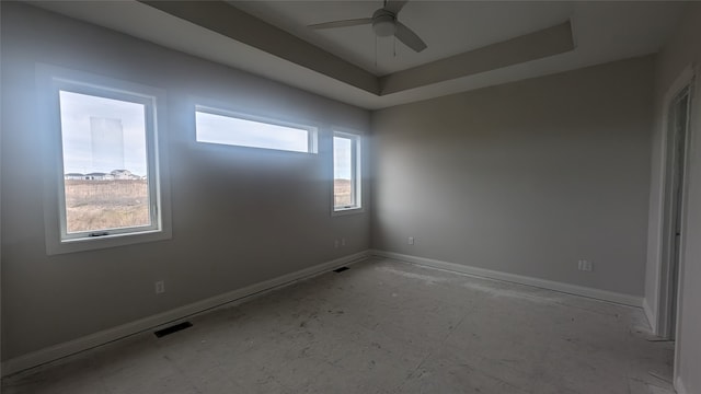 unfurnished room with ceiling fan, a healthy amount of sunlight, and a tray ceiling