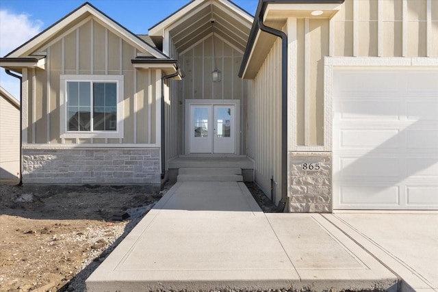 view of exterior entry featuring a garage, stone siding, board and batten siding, and french doors