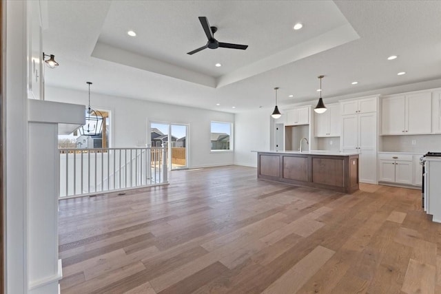 kitchen with pendant lighting, white cabinetry, a kitchen island with sink, a tray ceiling, and light hardwood / wood-style flooring