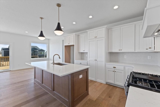 kitchen featuring hanging light fixtures, white cabinetry, sink, and an island with sink