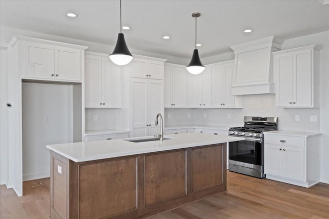 kitchen with pendant lighting, sink, white cabinets, gas range, and a center island with sink