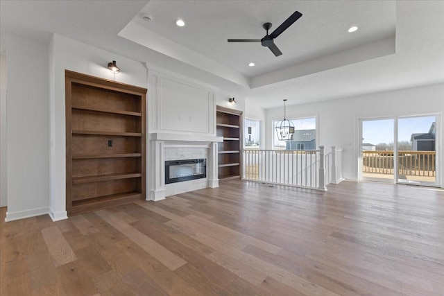 unfurnished living room featuring a raised ceiling, ceiling fan with notable chandelier, and hardwood / wood-style floors