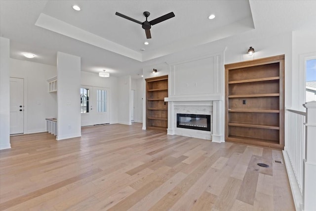 unfurnished living room featuring a healthy amount of sunlight, a fireplace, a raised ceiling, and built in features