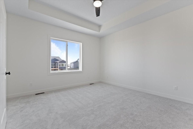 carpeted spare room with a raised ceiling and ceiling fan