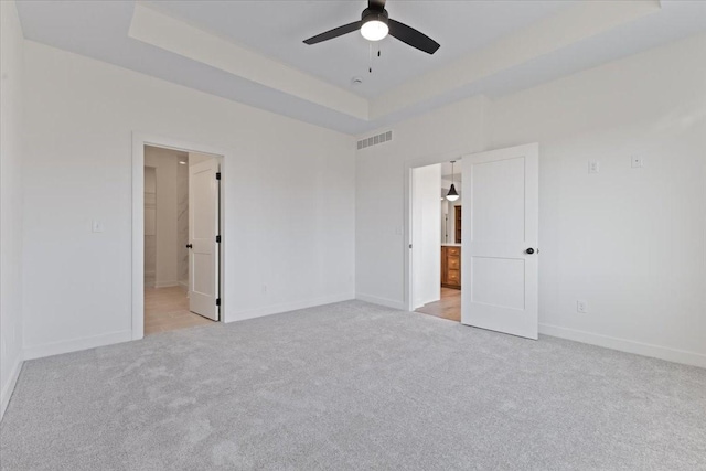 unfurnished bedroom featuring light carpet, a raised ceiling, ceiling fan, and ensuite bathroom