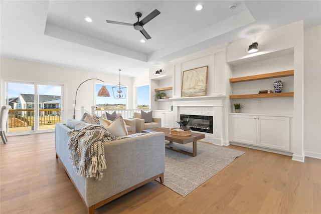 living room with light wood-type flooring, a fireplace, and a tray ceiling