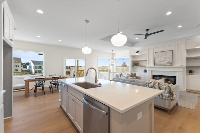 kitchen featuring pendant lighting, white cabinetry, sink, stainless steel dishwasher, and a center island with sink