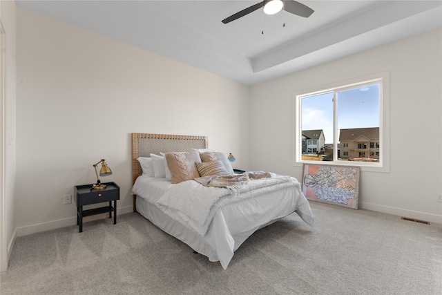 carpeted bedroom featuring ceiling fan and a raised ceiling