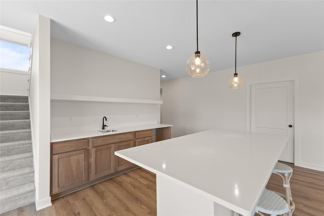 kitchen with a kitchen island, light hardwood / wood-style floors, sink, hanging light fixtures, and a breakfast bar area